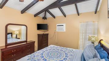 A bedroom with a bed, dresser, TV, and window with curtains.