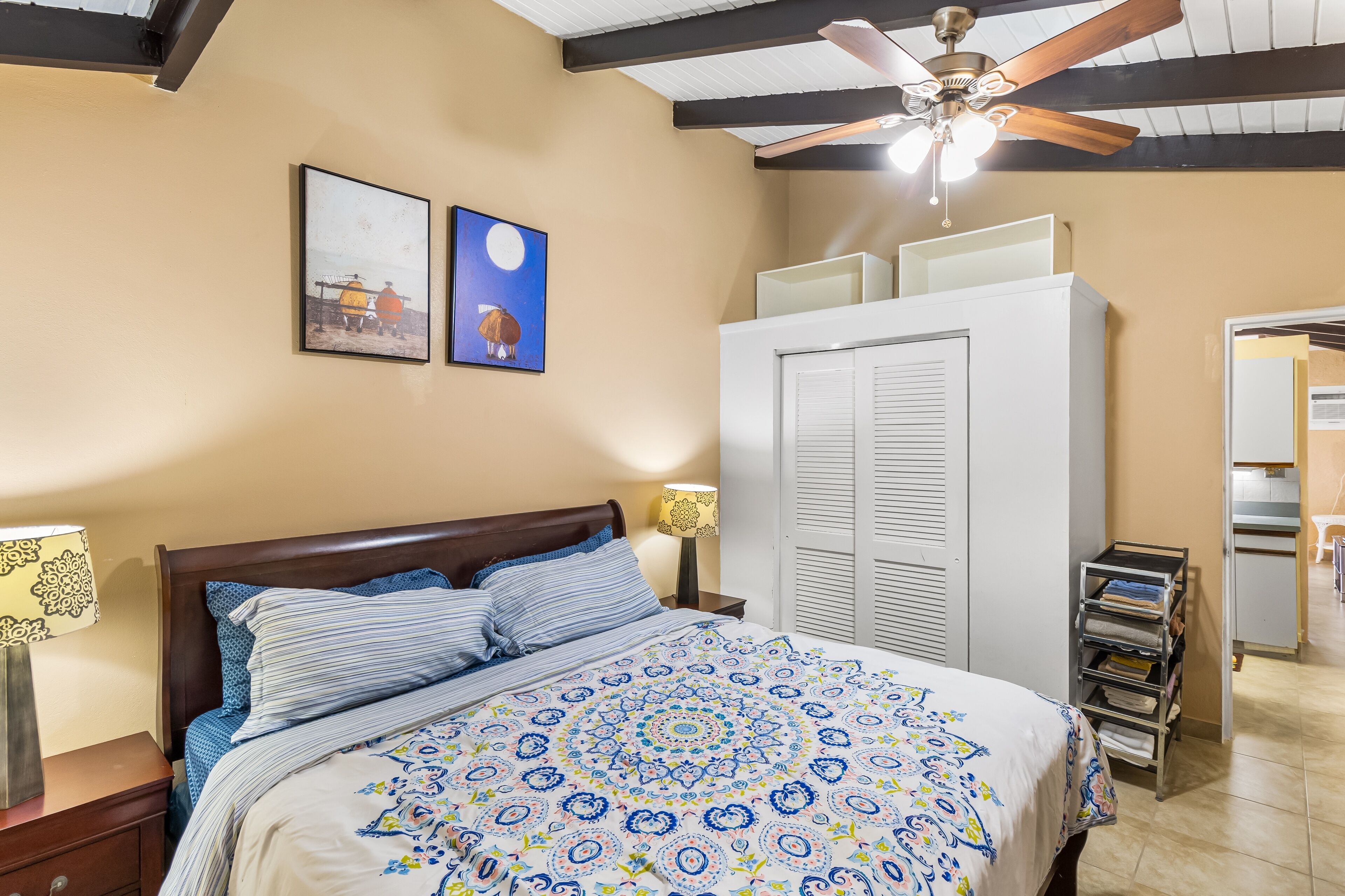 A bedroom with a bed, a nightstand, a lamp, a wardrobe, and a ceiling fan.