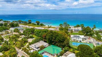 An aerial view of a coastal resort with a large pool, tennis court, and ocean views.