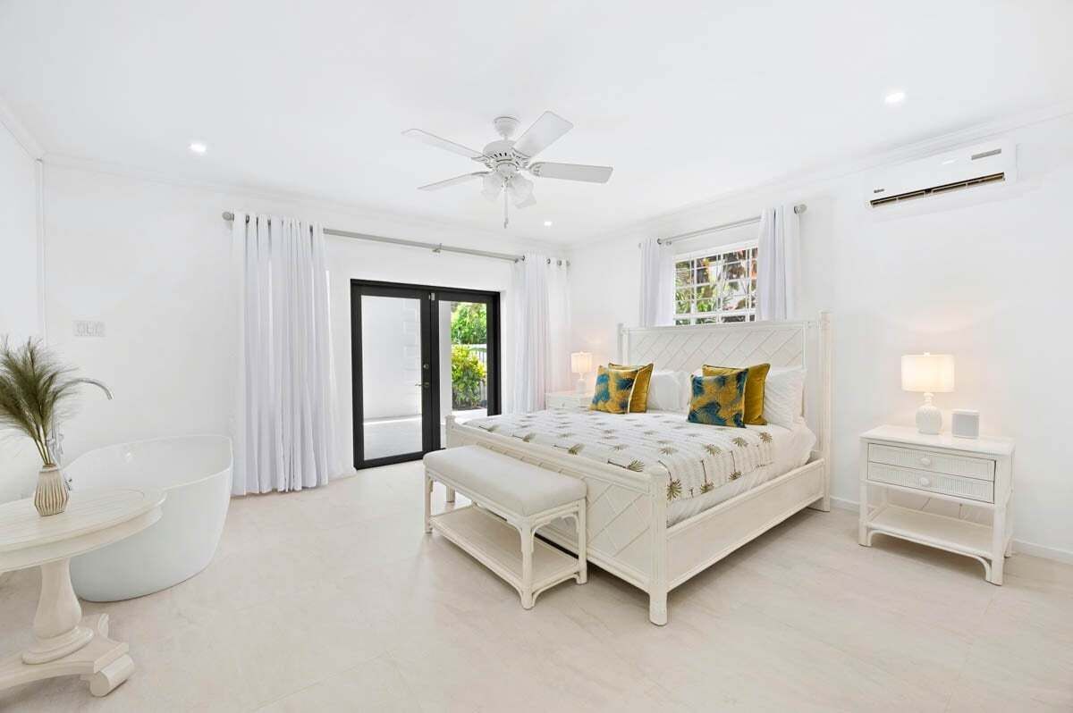 A bedroom with a bed, a bench, a nightstand, a ceiling fan, and a window.