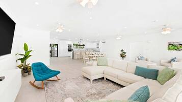 A spacious living room with a sectional sofa, a blue rocking chair, and a dining area in the background.