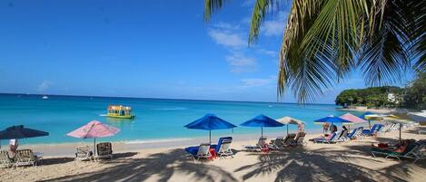 A beach with sun loungers and umbrellas, a clear blue sky, and a boat in the water.