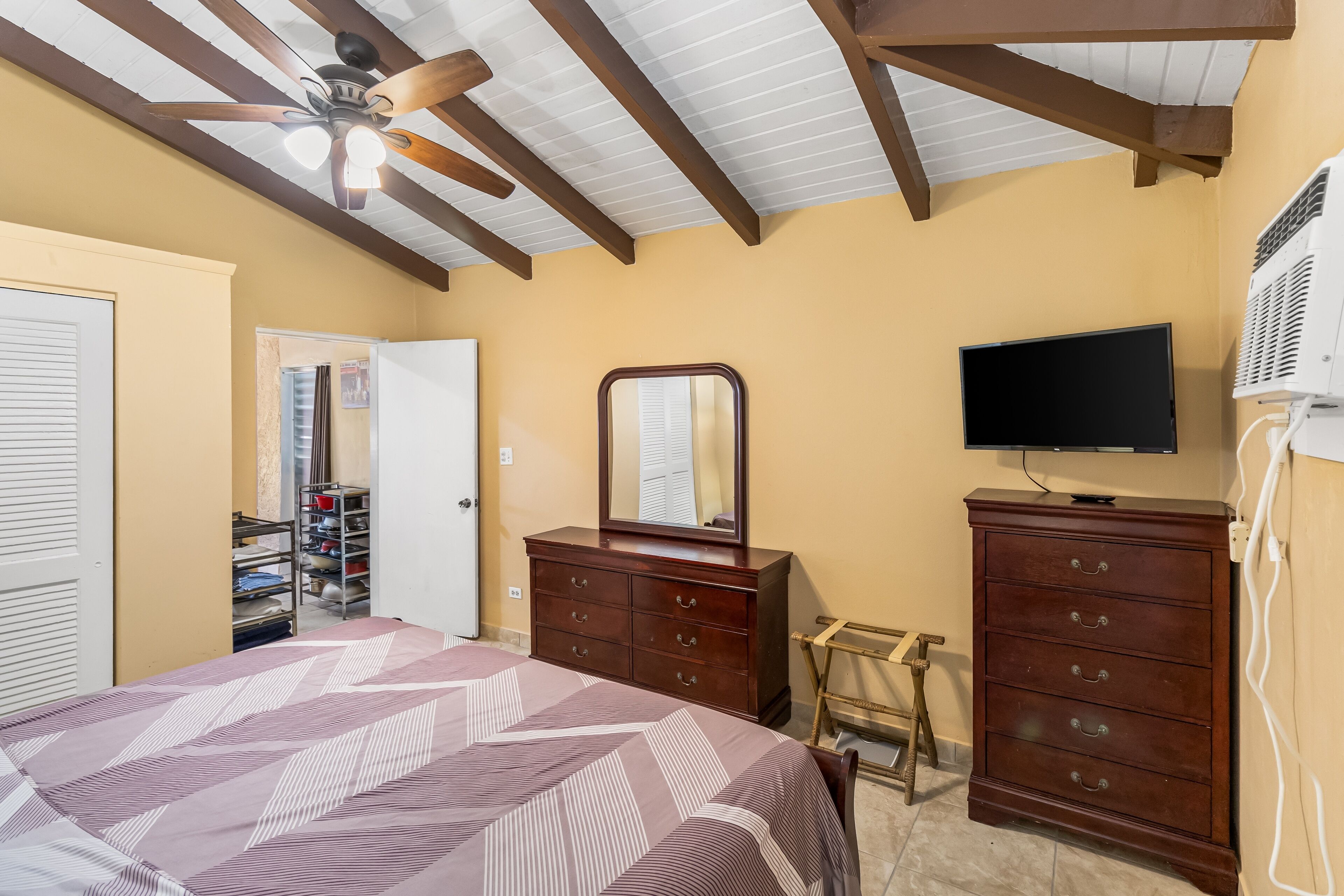 A bedroom with a bed, a dresser, a television, and a ceiling fan.