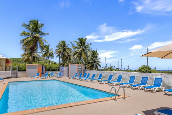 A swimming pool with blue lounge chairs, palm trees, and a clear sky. - Caribbean View Style 1 Bedroom Condo by RedAwning (Christiansted)