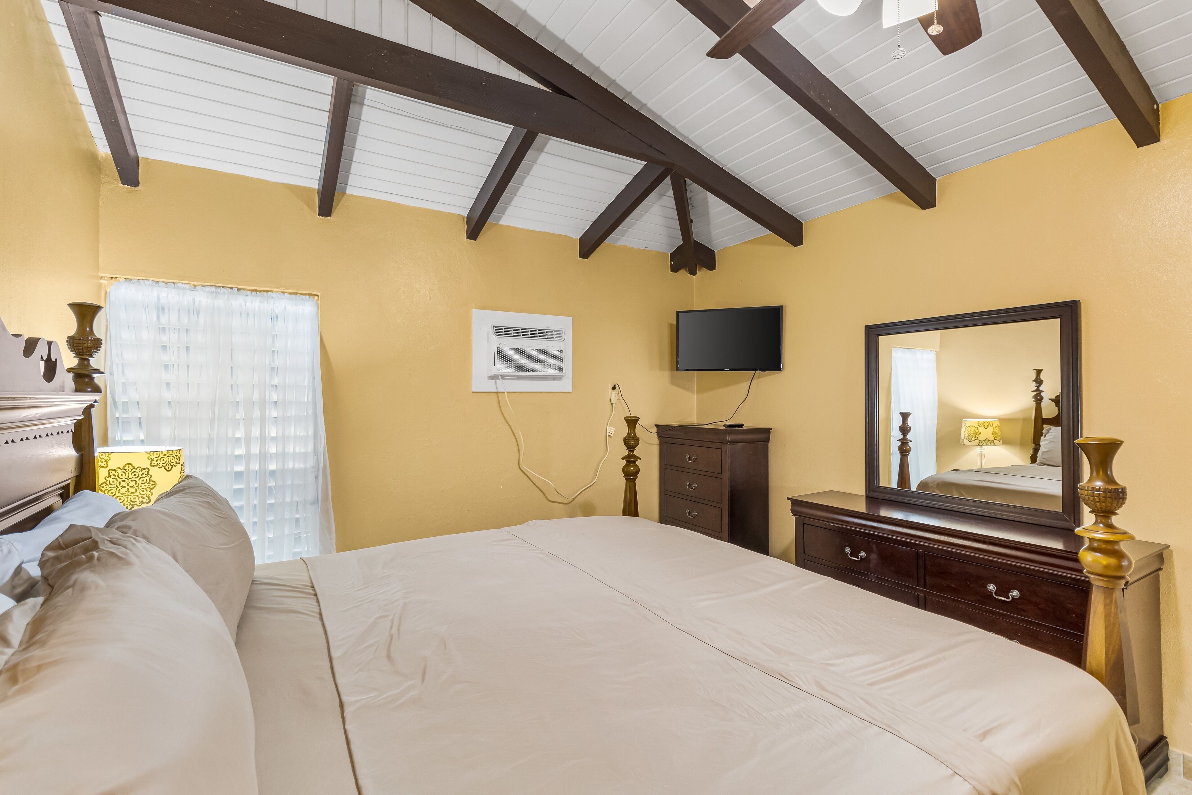 A bedroom with a bed, dresser, TV, and a ceiling fan.