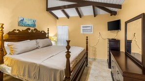 Une chambre avec un lit en bois, un ventilateur de plafond, une télévision et une commode.