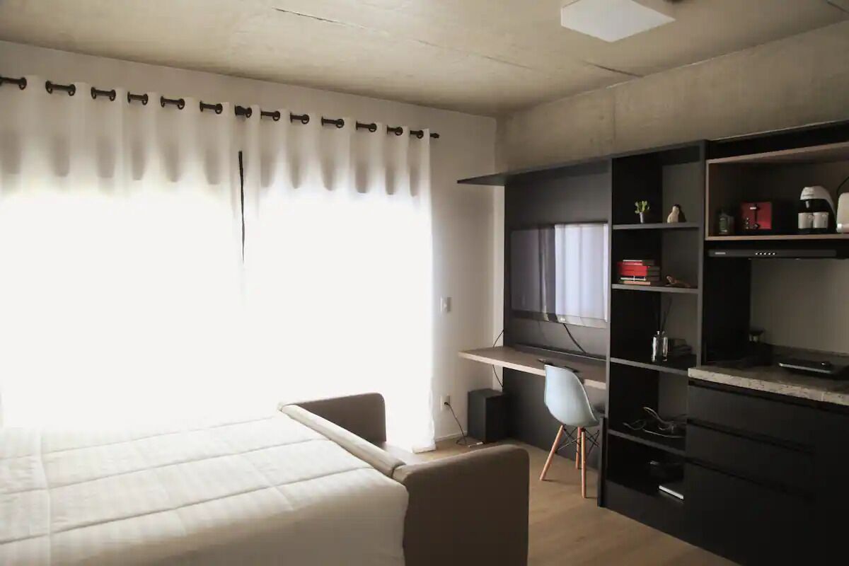 A room with a bed, a desk, a chair, a TV, and shelves with various items.