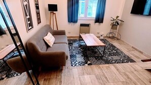 A living room with a sofa, a coffee table, a TV, and a window with curtains.