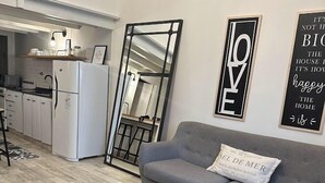 A modern living room with a grey sofa, a wooden coffee table, patterned floor tiles, and a kitchen area in the background.