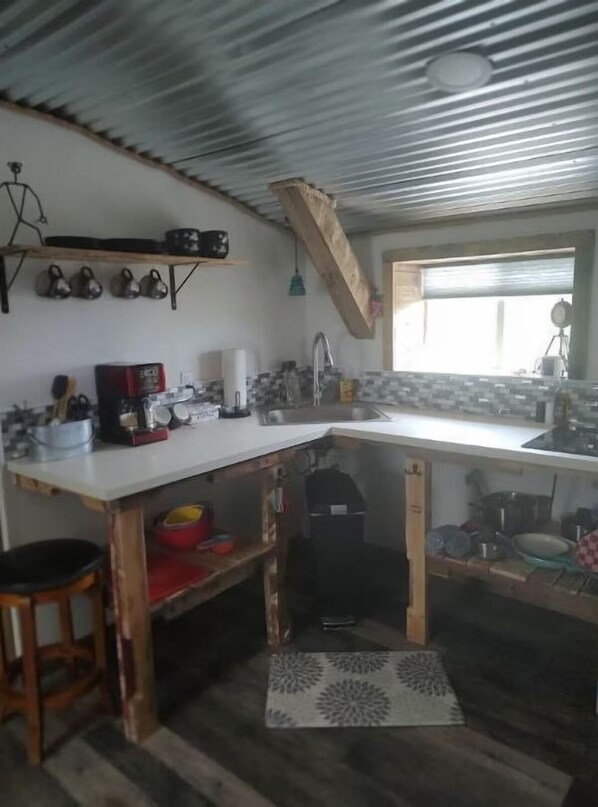 A compact kitchen with a white countertop, a wooden stool, and a patterned rug. - The Boulderdash Bird House studio apt! Wonderful tree top setting, in nature! (Bandera)