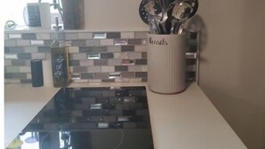 A kitchen with a black stove, a utensil holder, and a clock on the wall.