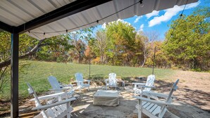 Eine Terrasse im Freien mit Adirondack-Stühlen und einem Steintisch, umgeben von einer Steinmauer und einer Rasenfläche mit Bäumen.