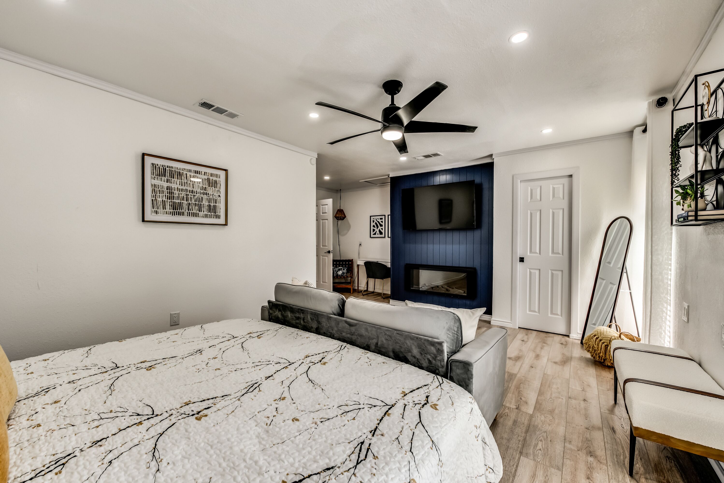 A bedroom with a bed, a ceiling fan, a TV, and a fireplace.