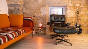 Una habitación acogedora con sofá, sillón de cuero, una guitarra y una pared de piedra.