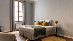 Un dormitorio con una cama grande, un tapete redondo tejido, una mesita de noche con lámpara y una ventana con cortinas.