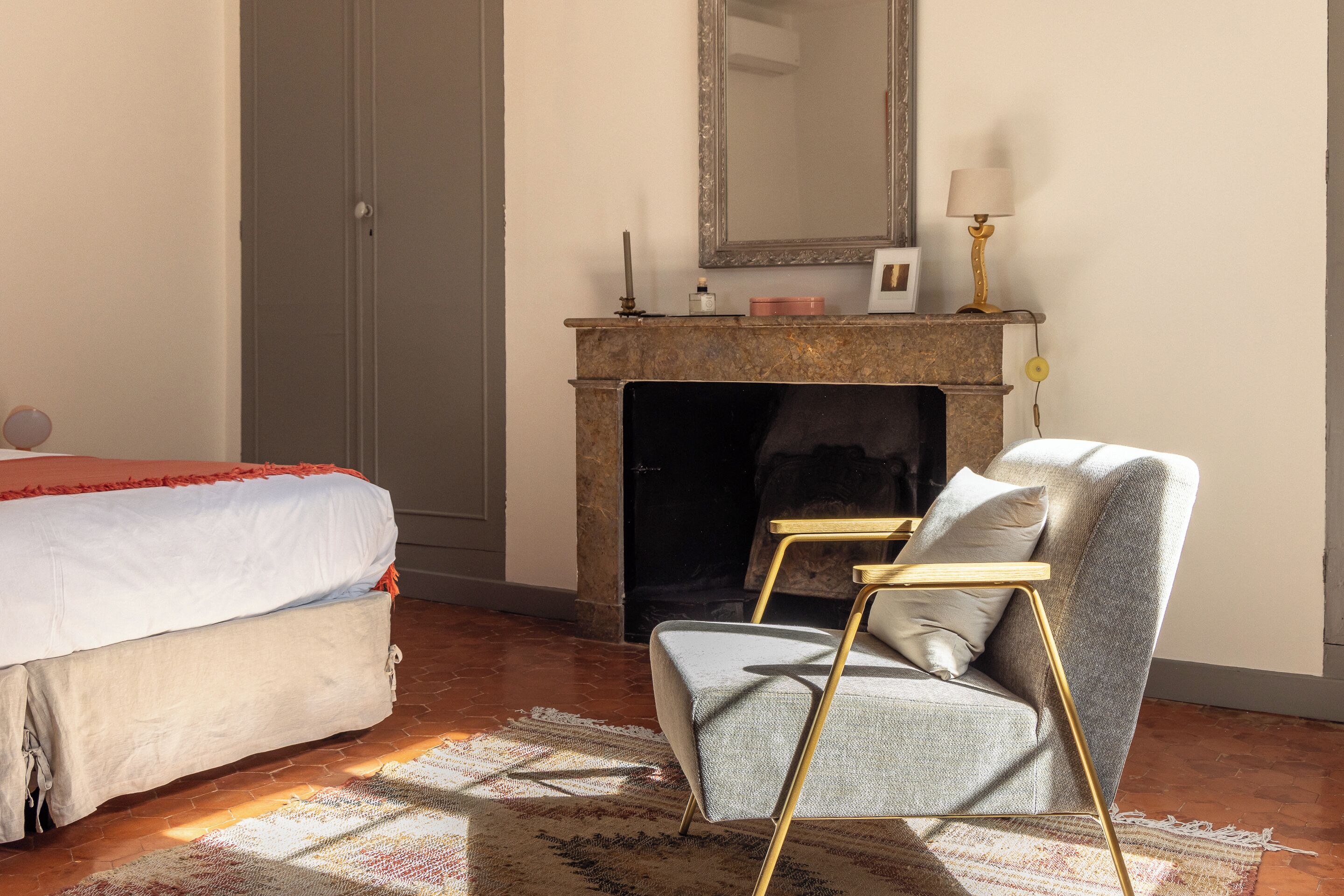 A bedroom with a bed, a chair, a fireplace, and a mirror.