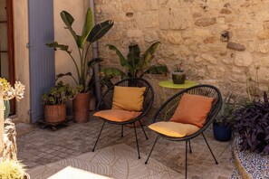 Un patio con dos sillas de mimbre, una mesita redonda y plantas en macetas.
