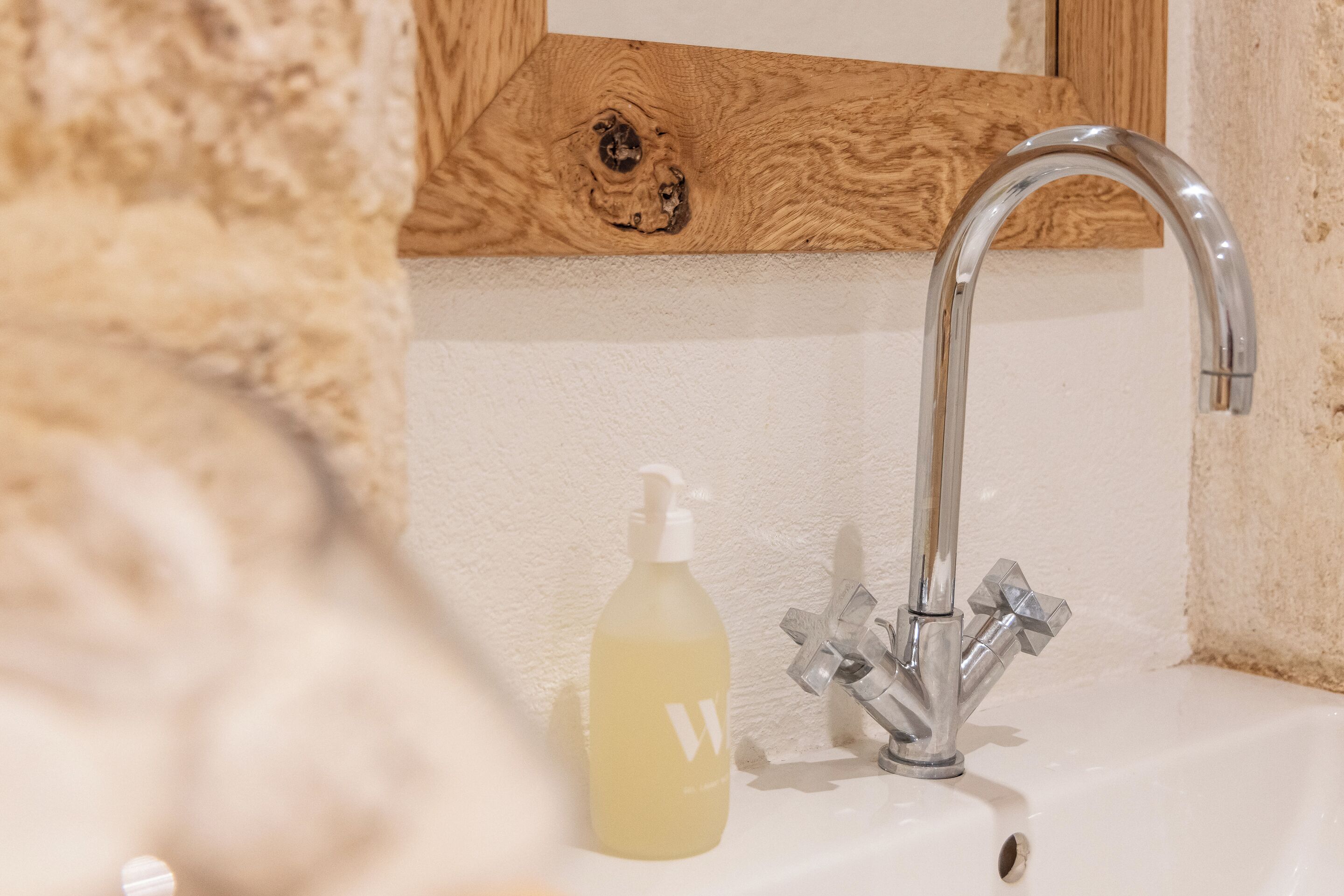 A bathroom with a wooden vanity, a modern faucet, and a bottle of liquid soap.