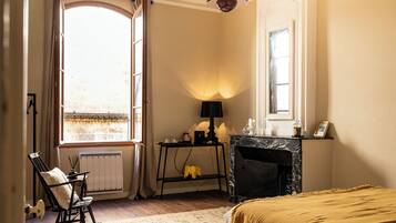 Una habitación con chimenea, un sillón mecedor, una mesa con lámpara y un ventanal grande.