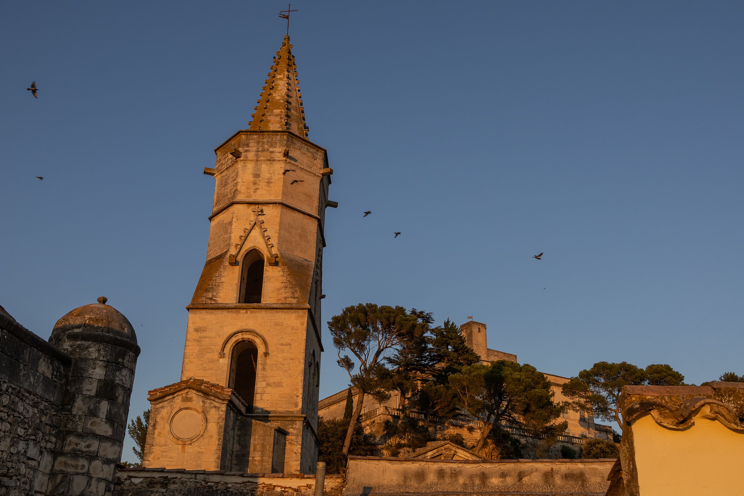 A historic church with a tall bell tower and a dome, surrounded by stone walls and trees.