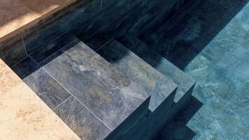 A pool with dark and light tiles, a clear water surface, and a stone ledge.