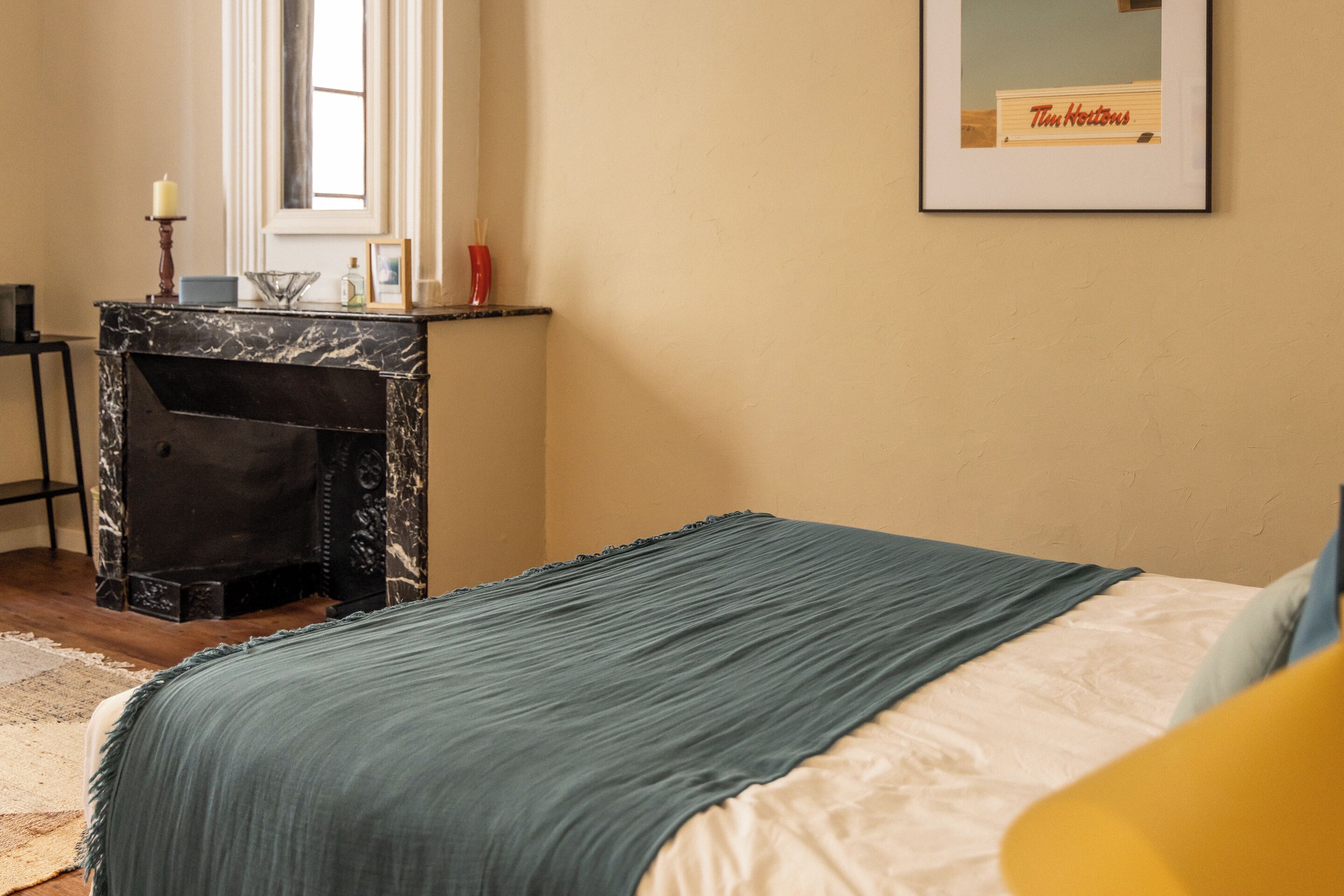 Une chambre à coucher comprenant un lit, une table de chevet, une cheminée en marbre, un tableau encadré accroché au mur et une fenêtre.