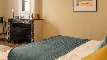 Une chambre à coucher comprenant un lit, une table de chevet, une cheminée en marbre, un tableau encadré accroché au mur et une fenêtre.