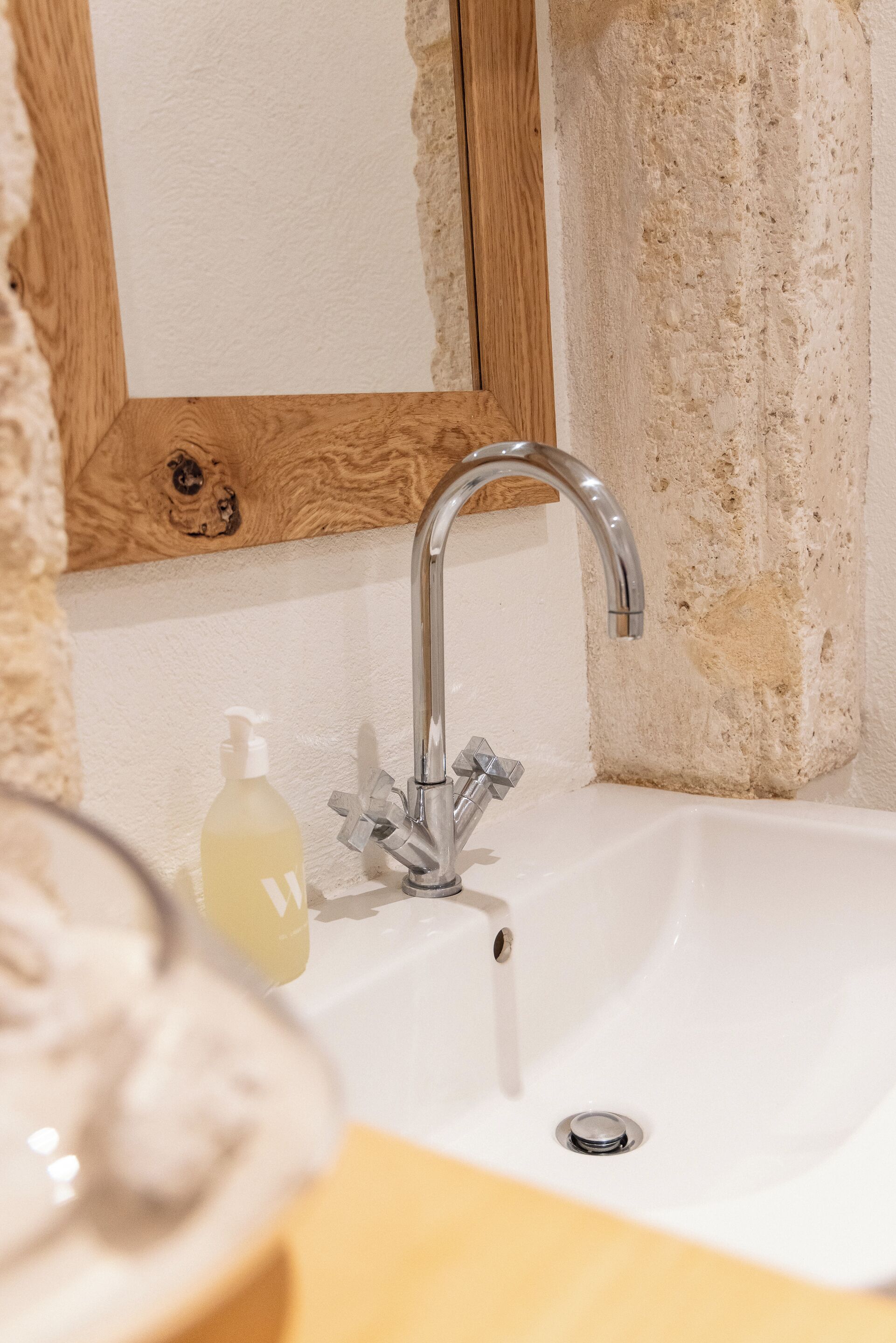 A bathroom sink with a modern faucet, a wooden-framed mirror, and a bottle of hand soap.