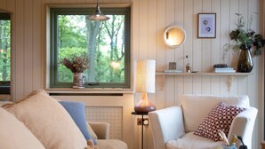 A cozy living room with a sofa, armchair, and a table with books and a vase. - Luxury Treehouse with amazing views in 100 acres of secluded private Land. (Hereford)
