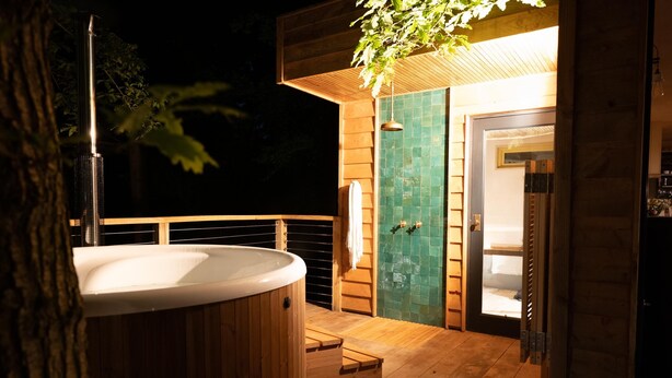 A wooden deck with a hot tub, a shower, and a door leading to a room. - Luxury Treehouse with amazing views in 100 acres of secluded private Land. (Hereford)