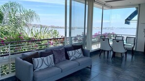 Ein Balkon mit einer Sitzecke, der auf ein Gewässer und Grünflächen blickt.