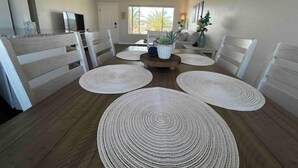 Un coin repas avec une table en bois, des chaises blanches et des sets de table en fibres tressées.