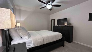 Une chambre à coucher comprenant un lit, une commode, un téléviseur, un ventilateur de plafond et une lampe.