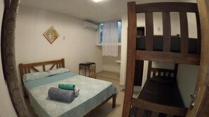 Een kamer met een bed, een houten stapelbed, een klein tafeltje en een raam met gordijn.