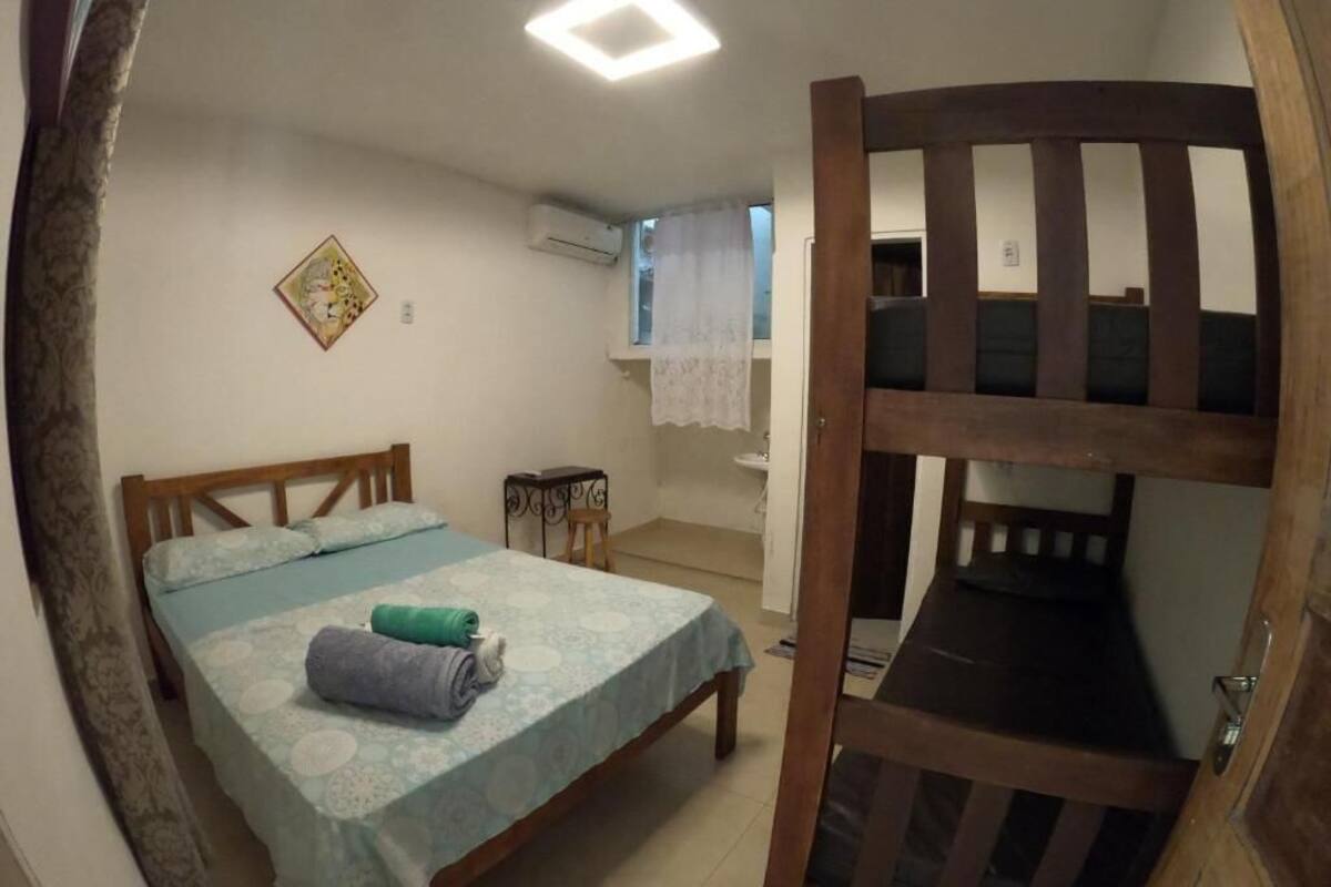 Une pièce comprenant un lit, un lit superposé en bois, une petite table et une fenêtre avec un rideau.