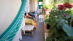 Een hangmat en een bankje in een smalle buitenpassage, met potplanten en een groene wand.