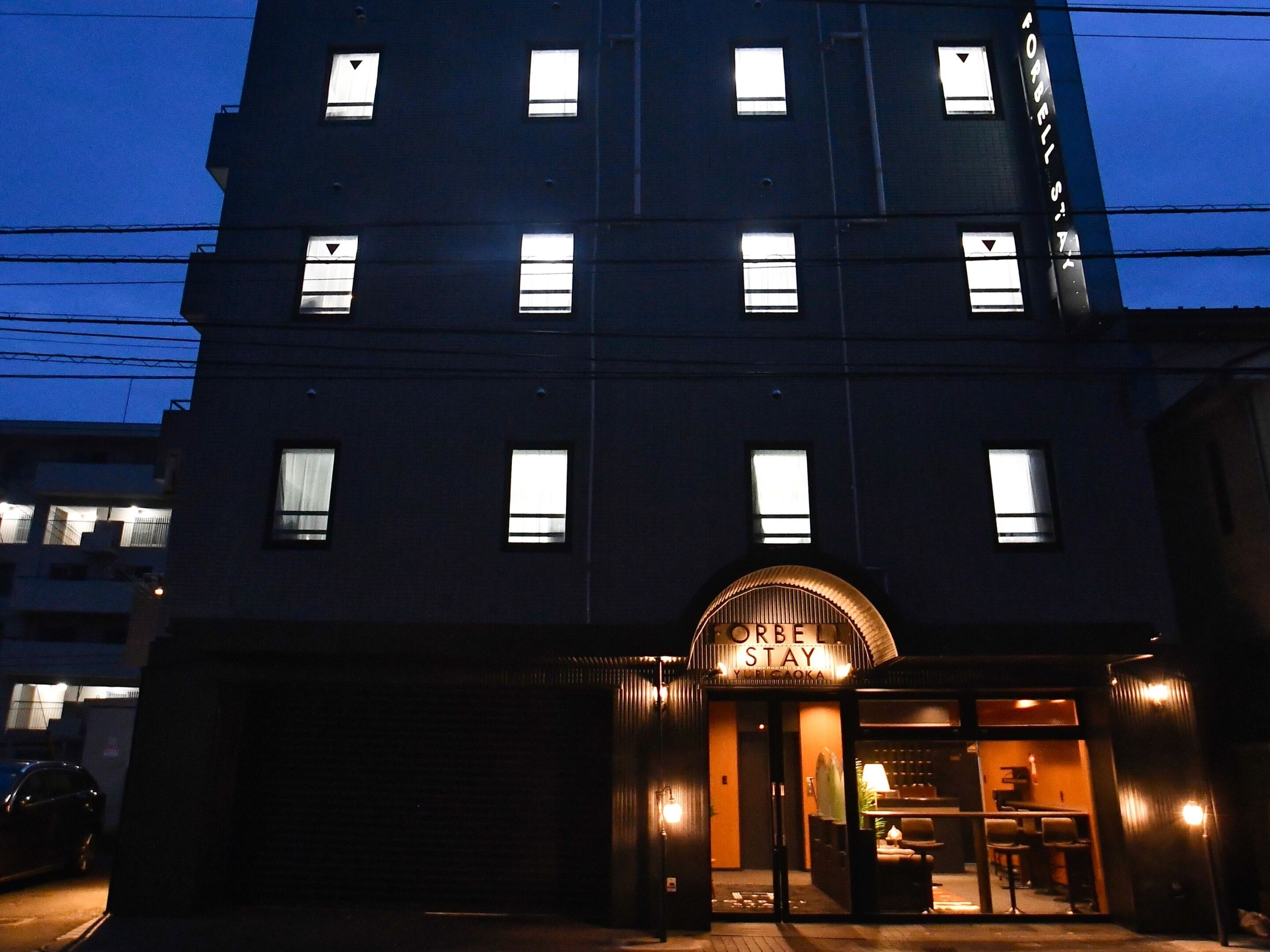 Un hôtel à plusieurs étages, avec des fenêtres illuminées et une enseigne indiquant « FOREST STAY ».