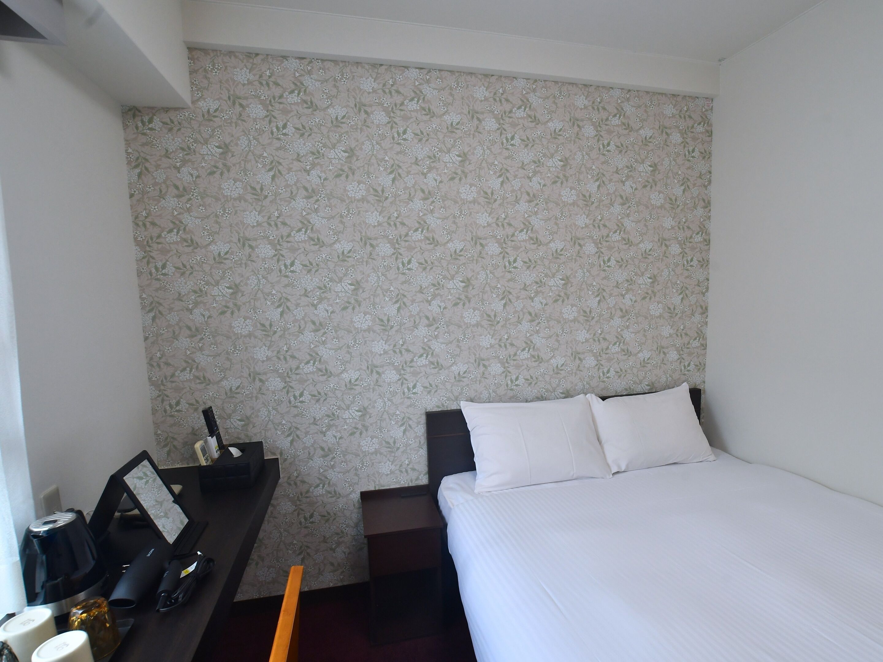 A hotel room with a bed, a desk with a coffee maker, and a small table with a picture frame.