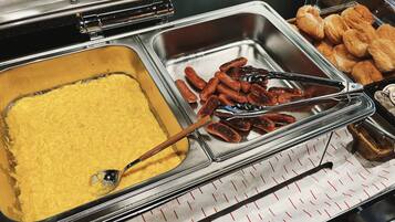 A buffet with a variety of food items including a tray of yellow custard, sausages, and pastries.