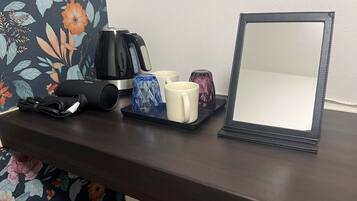 A dark wooden table with a black kettle, a blue glass, a white mug, a pink glass, and a black speaker.