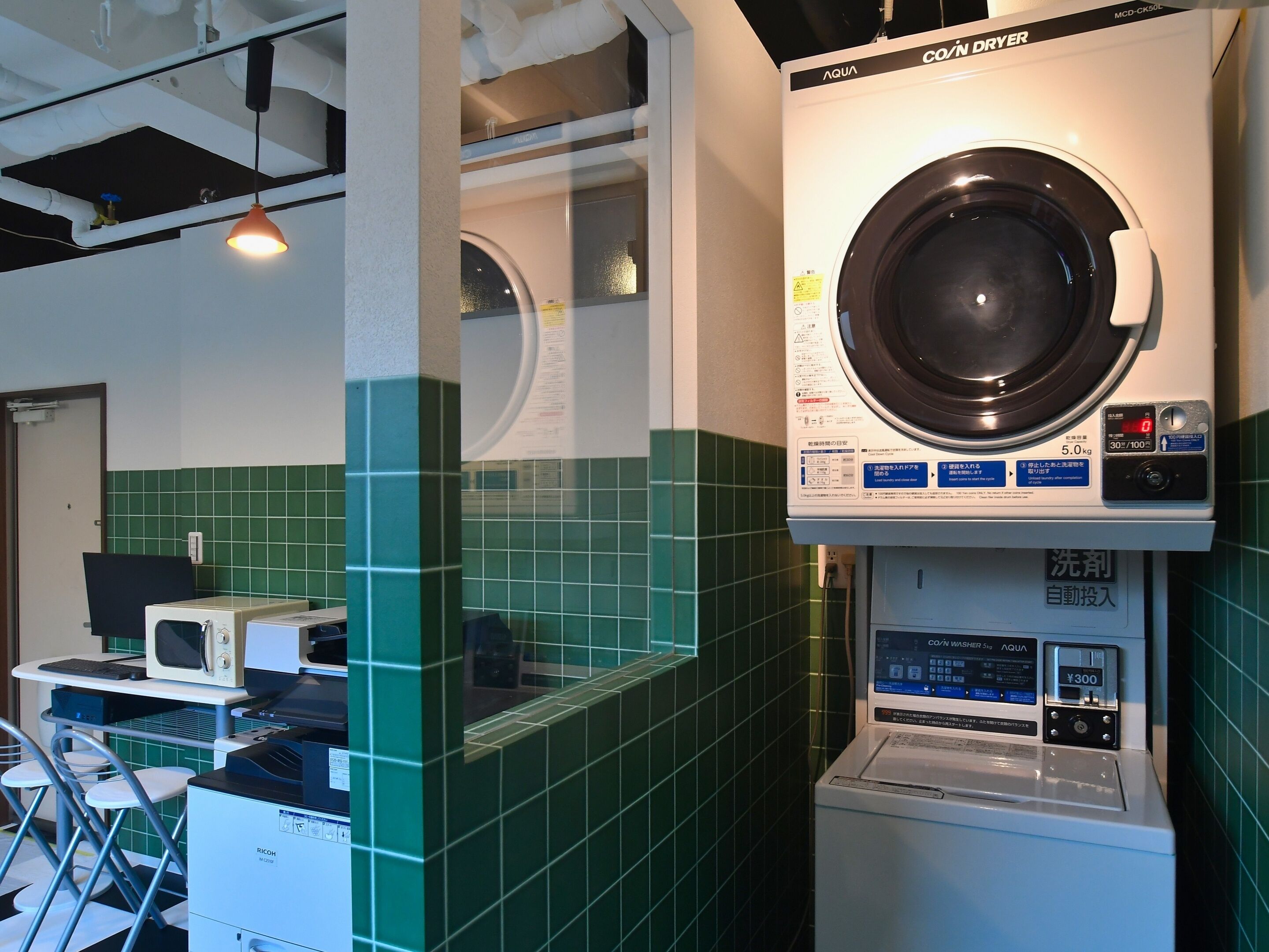 Une laverie équipée d’un lave-linge et d’un sèche-linge à chargement frontal, d’un four à micro-ondes et d’un petit coin salon avec des tabourets.