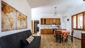 Eine moderne Küche mit Holzausbau, einem Essbereich mit Tisch und Stühlen sowie ein schwarzes Sofa mit gemustertem Kissen.