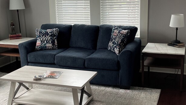 A living room with a dark blue sofa, two white lamps, a white coffee table, and a ceiling fan.