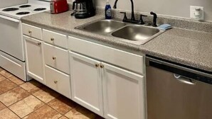 A kitchen with white cabinets, a stove, a sink, and a coffee maker.