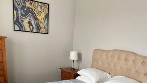 A bed with a striped bedspread, a wooden nightstand with a lamp, and a marble artwork on the wall.