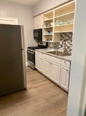 Una cocina compacta con armarios blancos, un refrigerador de acero inoxidable, un microondas y un salpicadero de azulejos.