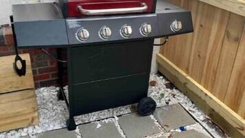 Un barbecue portatif doté de quatre brûleurs et d’un thermomètre, installé sur une terrasse carrelée en pierre.
