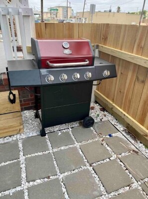 Ein tragbarer Grill mit vier Brennern und einem Thermometer, platziert auf einer Terrasse mit Steinplatten.