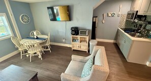 Een compacte woonruimte met een eethoek, een bank, een keuken met een magnetron, en een aan de muur bevestigde televisie.