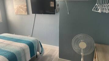 A bedroom with a bed, a wall-mounted TV, and a standing fan.
